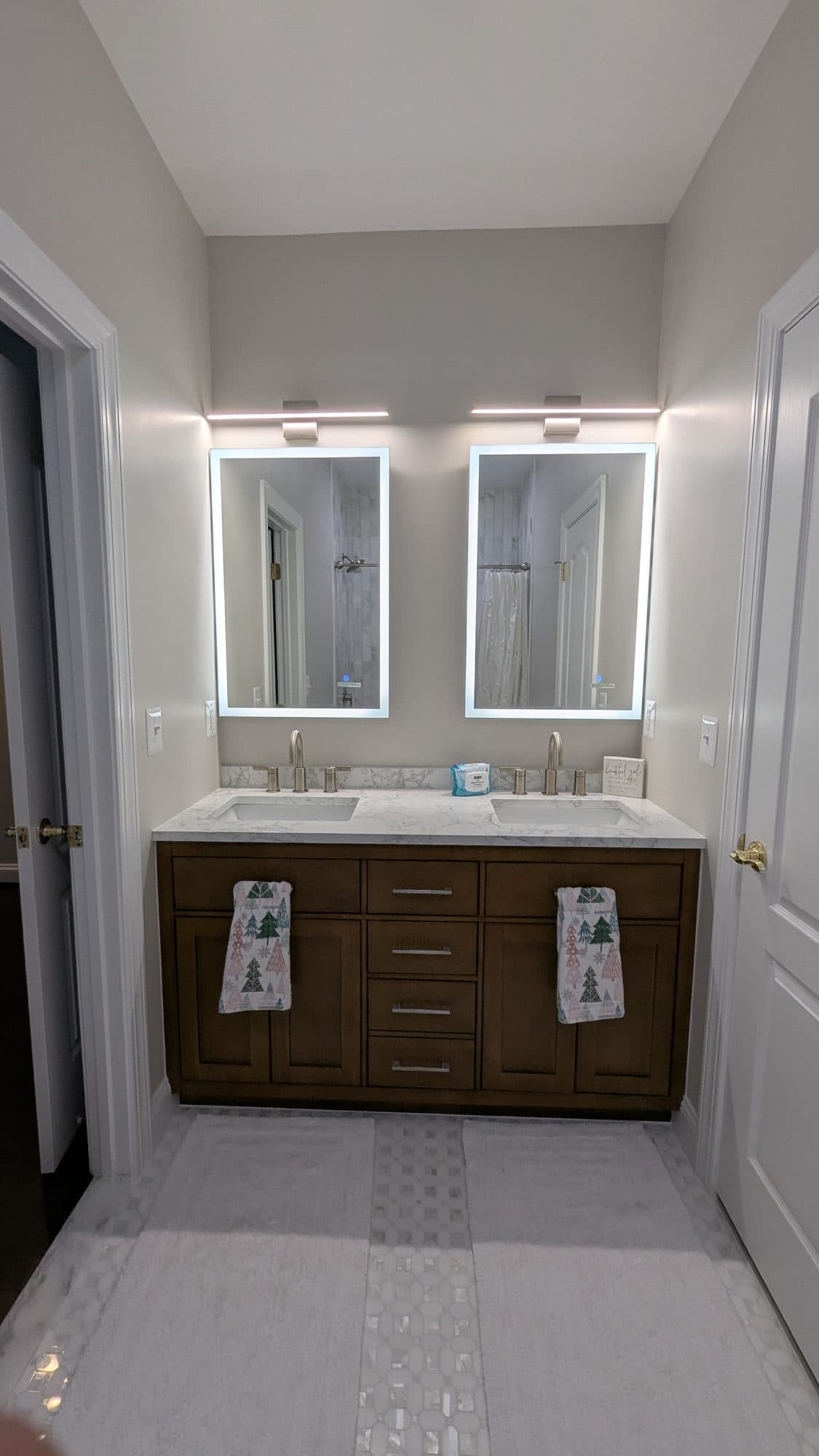 Double vanity with backlit mirrors, quartz countertop, and stained wood cabinetry