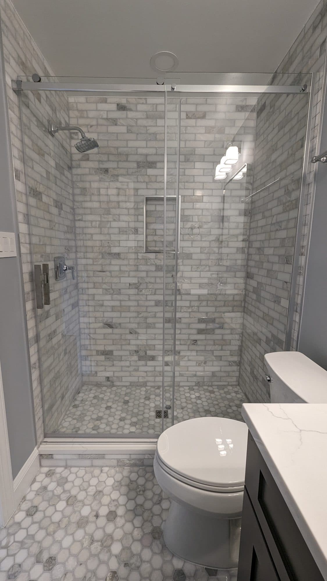 Frameless glass walk-in shower with marble subway tile and a built-in niche