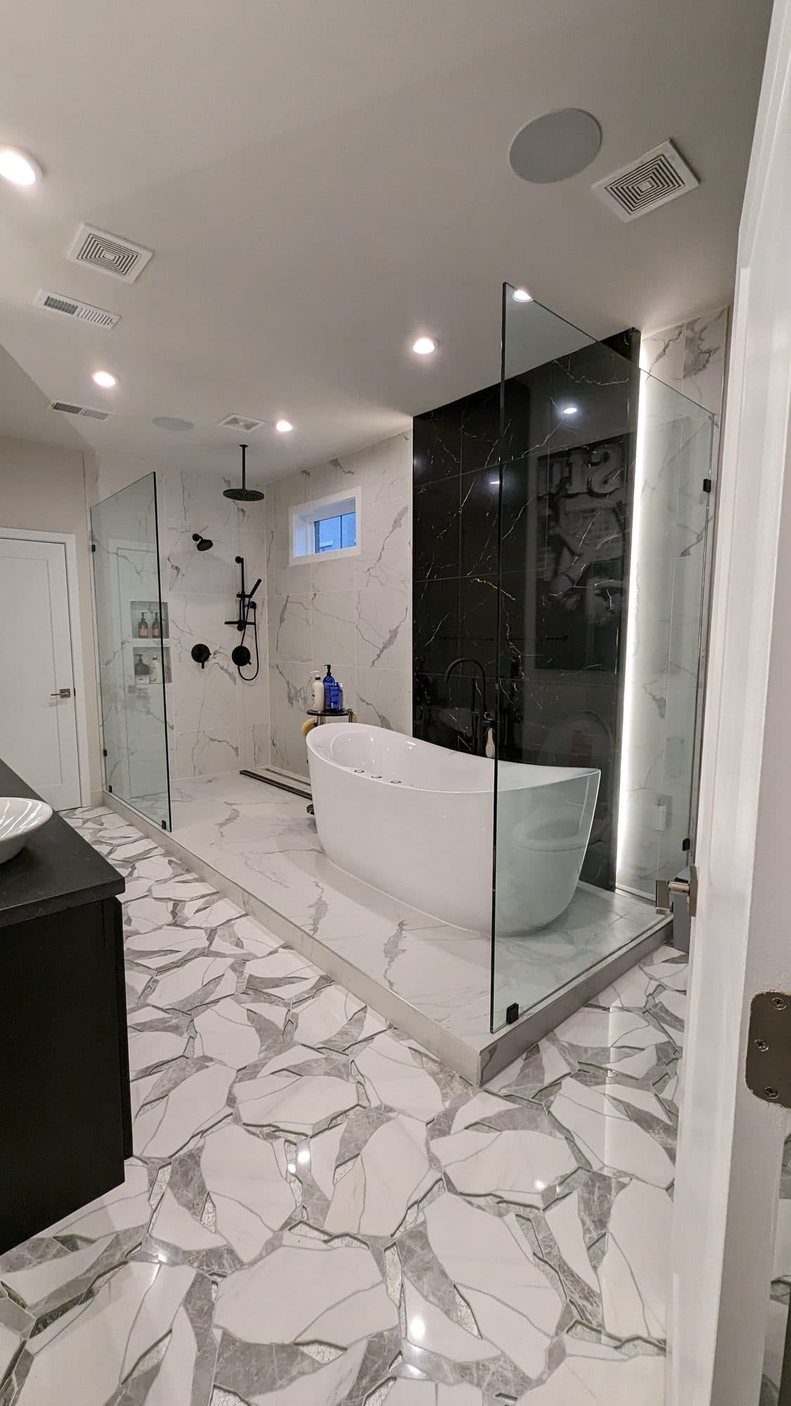 Luxury primary bathroom with a freestanding soaking tub, black marble accent wall, and glass walk-in shower