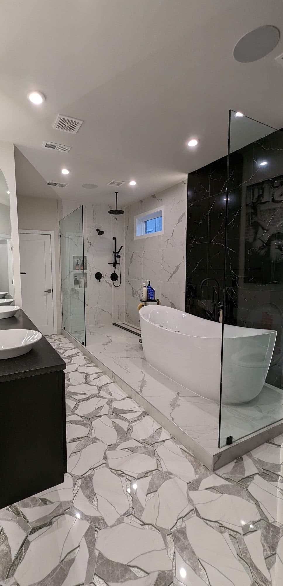 Luxury primary bathroom with a freestanding soaking tub, black marble accent wall, and rainfall shower