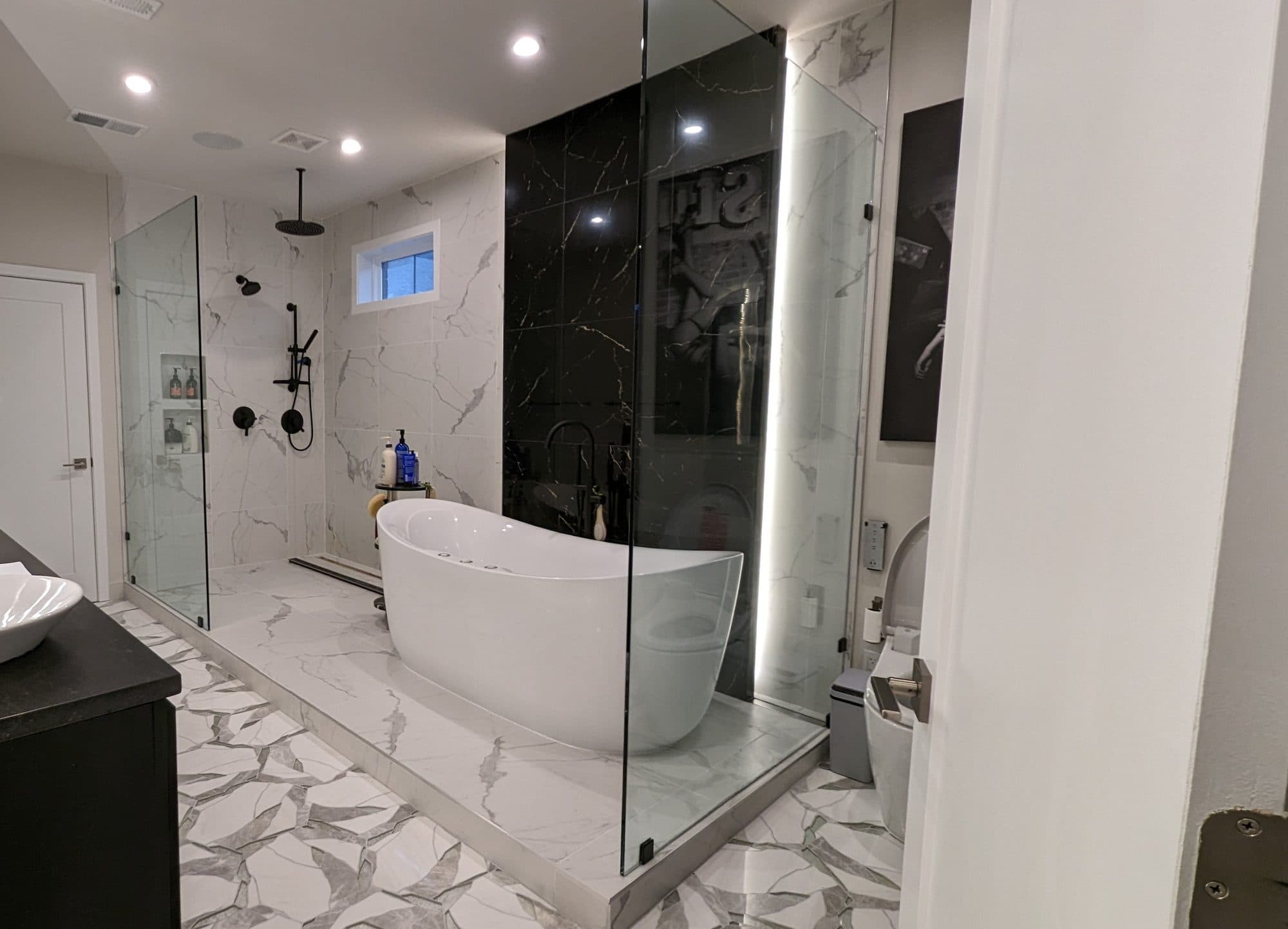 Wide view of a luxury primary bathroom with a freestanding tub, black marble accent wall, and glass shower enclosure